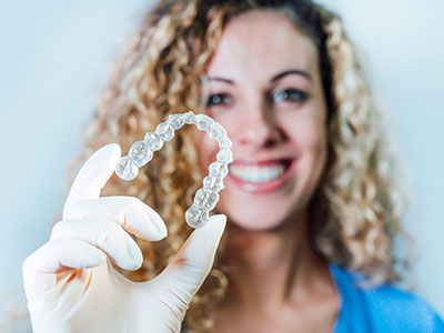 A woman holding a transparent dental retainer in her hand against a white background.